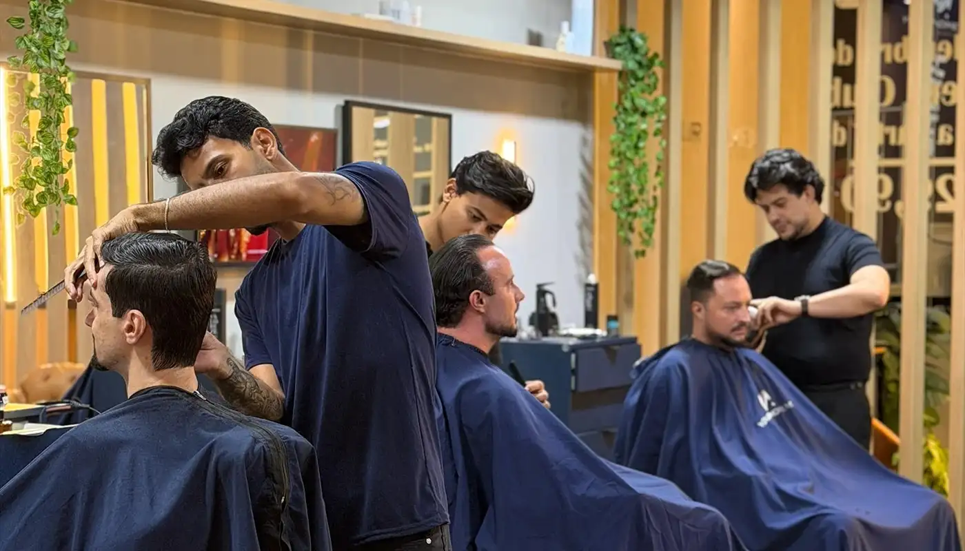 Três barbeiros da Your Moment atendendo clientes lado a lado no salão